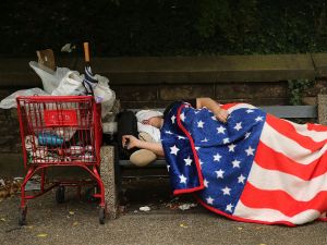 A homeless man sleeps under an American Flag blanket on a park bench in the Brooklyn borough of New York City.