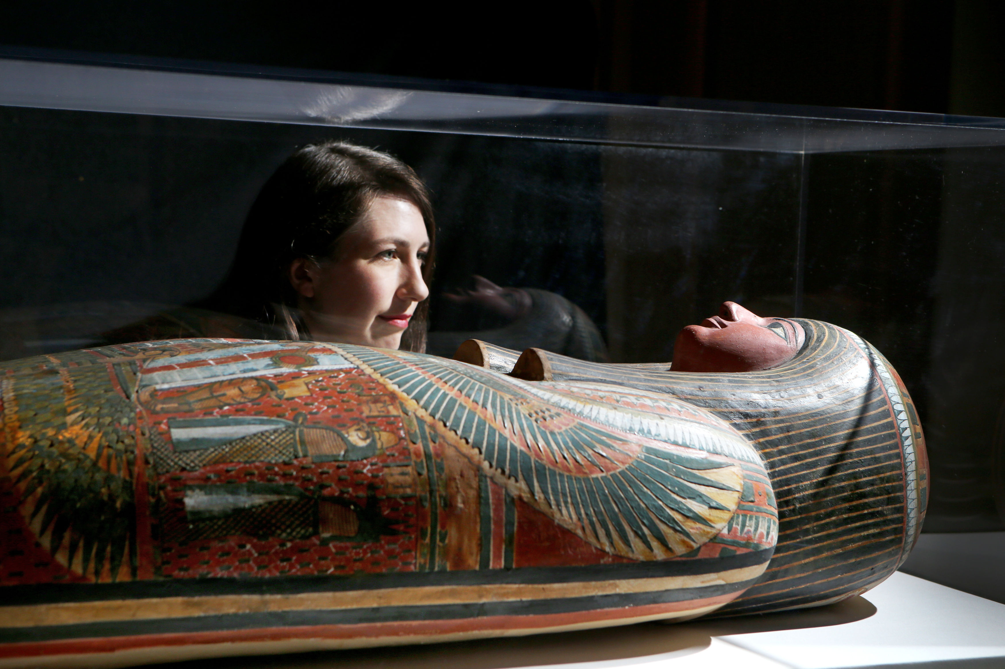 Museum curator looks at mummy encased in glass box at museum