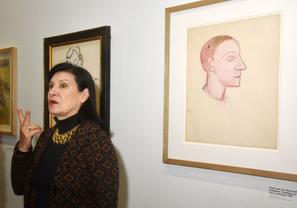 A woman stands in front of framed drawings of a man shown in profile