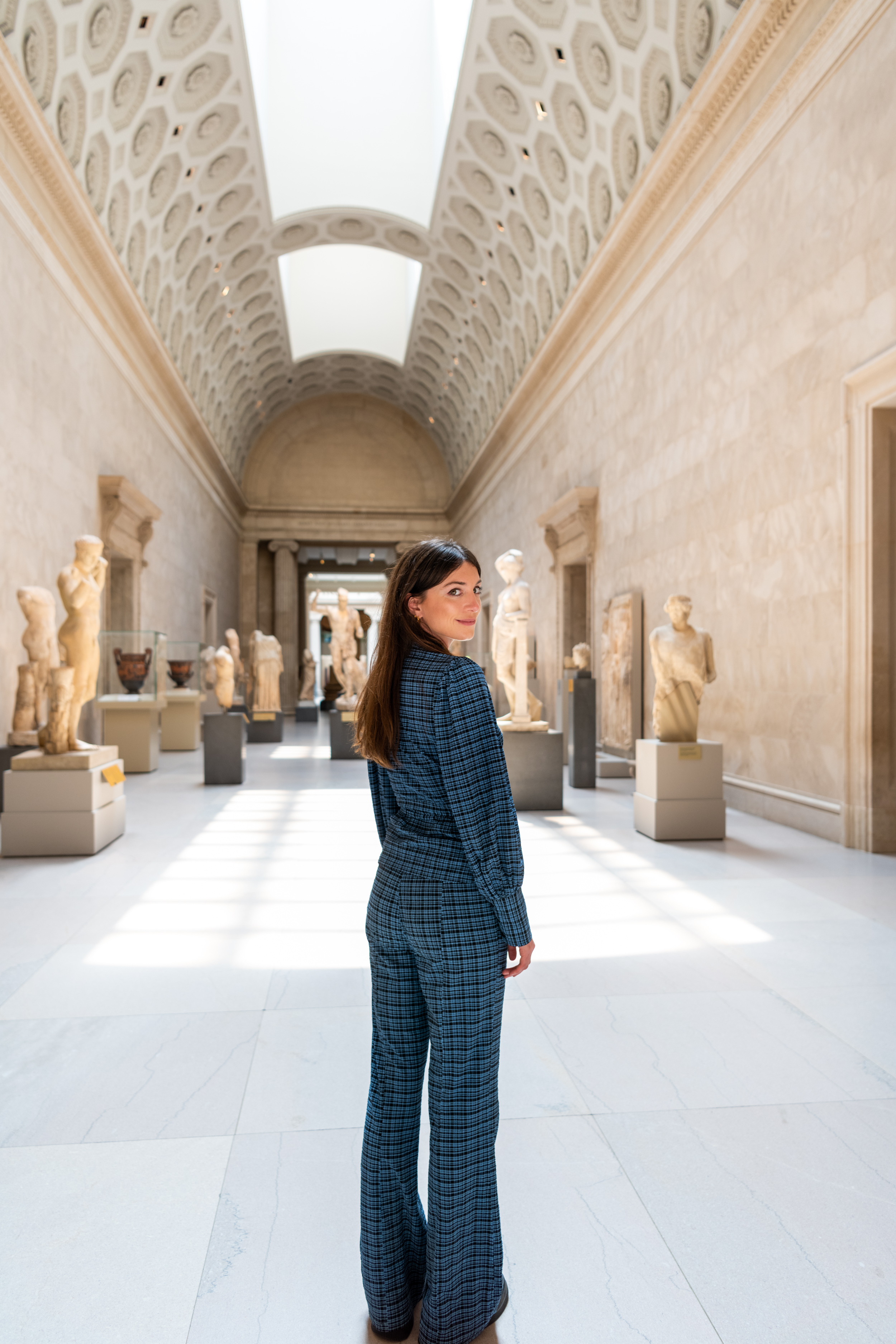 A woman wearing a blue suit stands in a long hallway with a skylight