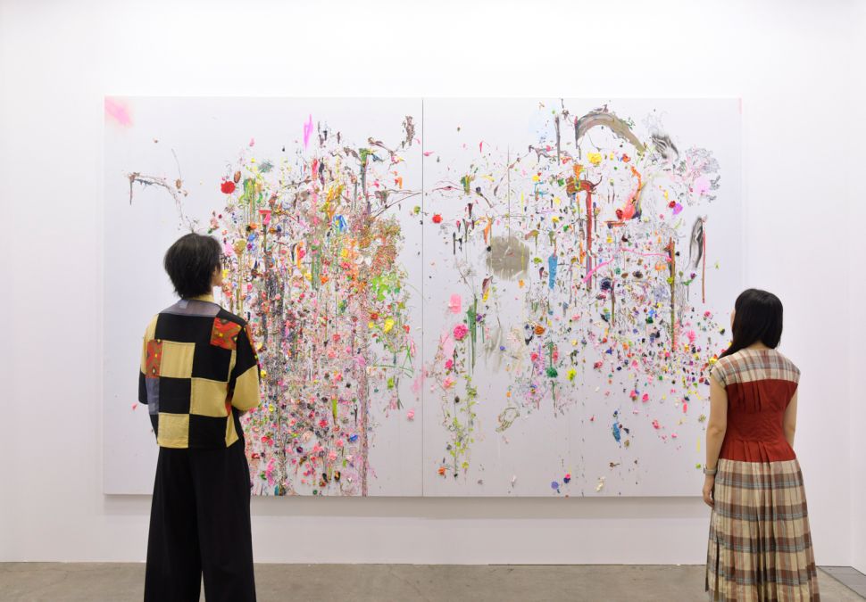 Two visitors standing in front of a white canvas punctuated by floral-like motifs
