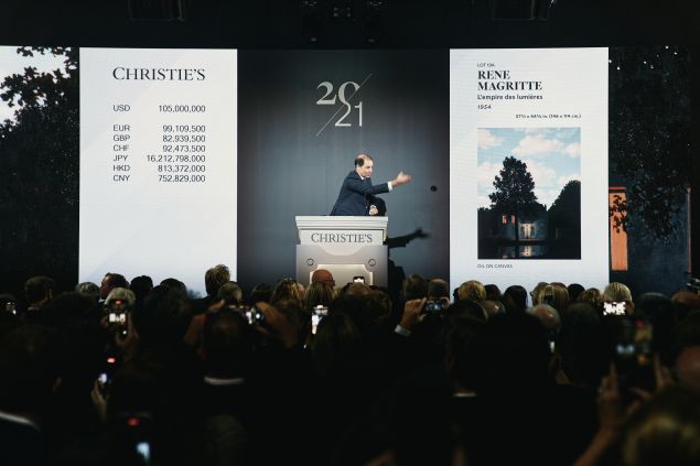 Image of a man with gavel leading a auction with a Magritte painting on the screen.