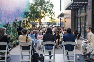 People attending a panel outdoor. View from the stage where four people are talking.