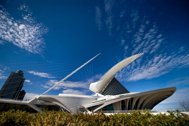 A striking futuristic looking white building with lots of jutting spines and curved wings looms in front of a deep blue sky with a smattering of clouds