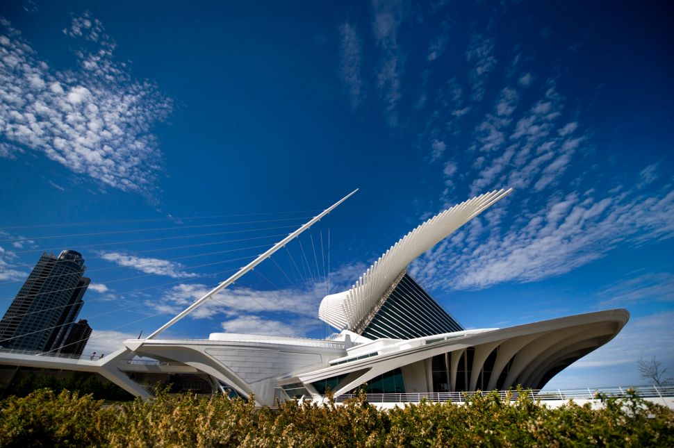 A striking futuristic looking white building with lots of jutting spines and curved wings looms in front of a deep blue sky with a smattering of clouds