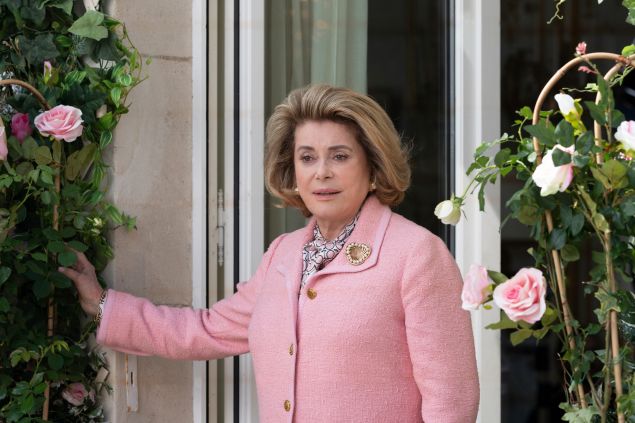 An older woman with short blonde hair poses in a pink tweed jacket.