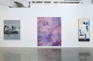 A contemporary art gallery wall featuring three paintings by different artists, including abstract compositions with purple, gray, and blue tones, blending textures and vibrant colors to evoke dynamic visual movement.