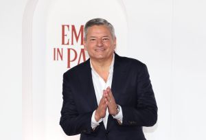 A smiling Ted Sarandos wearing a white shirt and a black blazer standing against a white background.