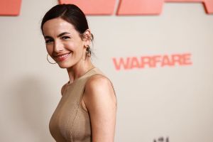 Camilla Belle smiling to the camera against a cream color background.