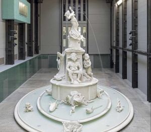 A large white sculptural fountain stands at the center of the Turbine Hall in Tate Modern, featuring allegorical figures and flowing water as part of Kara Walker’s 2019 installation Fons Americanus, referencing British colonial history.