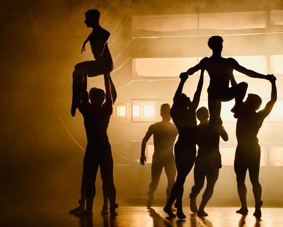 A group of dancers from Tabula Rasa Dance Theater perform a dramatic lift on stage, silhouetted against a glowing amber background in a scene from Border of Lights.